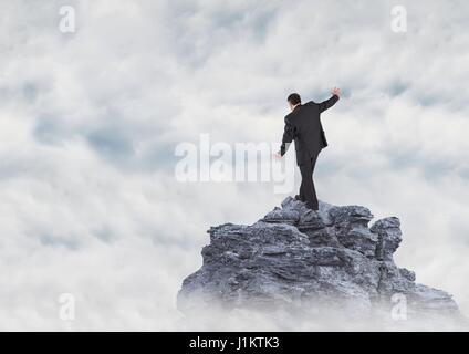 Digital composite of Business man walking up mountain peak in the clouds Stock Photo