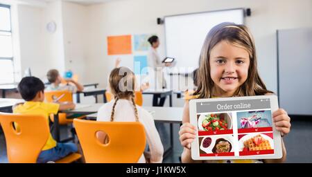 Digital composite of Happy girl holding digital tablet with restaurant site on screen in classroom Stock Photo