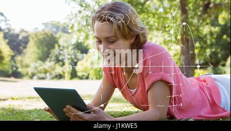 Digital composite of Female student using tablet PC while lying on grass Stock Photo