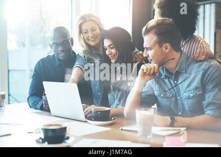 Woman showing coworkers something on laptop computer as they gather around a conference table Stock Photo