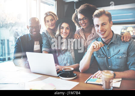 Smiling group of coworkers in small office seated around laptop computer and forms on conference table Stock Photo