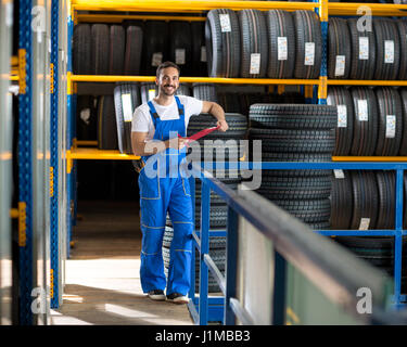 mechanic in blue uniform standing at stock tyre and holding a clipboard Stock Photo