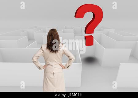 Digital composite of Rear view of businesswoman with hands on hips looking at question mark over maze Stock Photo