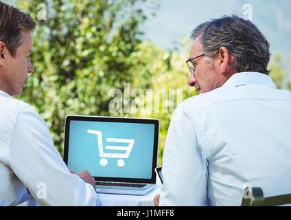 Digital composite of Two men using Laptop with Shopping trolley icon Stock Photo