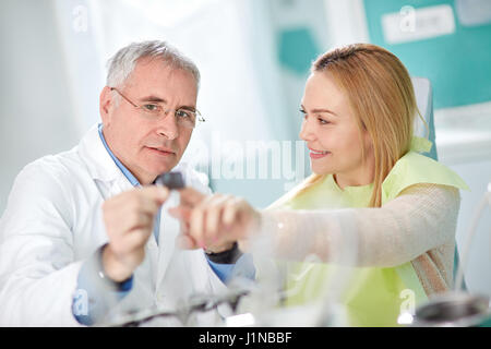 Nice young woman in dental chair and dentist talk about her snapshot on dental clinic Stock Photo