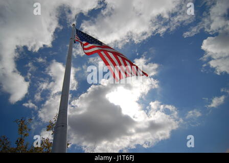 looking up flagpole at flag and blue skies and white clouds Stock Photo