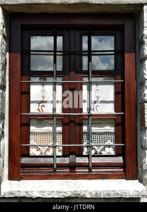 Wooden window with elegant curtains, sky reflection and steel bars on the stone house. Stock Photo