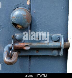 Old sliding bolt on painted wooden door below rusting round handle Stock Photo