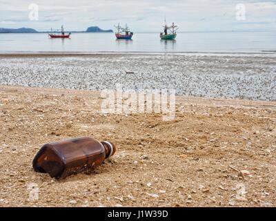A brown glass bottle thrown away in the beautiful sand beach as garbage, waste on sand, polluted sea, Dolphin Bay, Prachuap Khiri Khan,Thailand Stock Photo