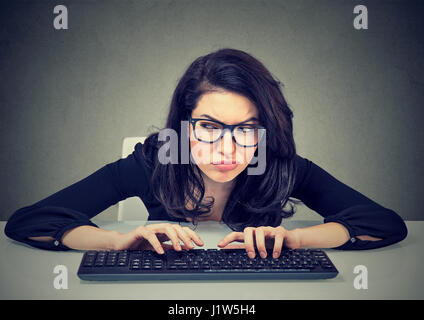 Crazy looking nerdy woman typing on the keyboard wondering what to reply plotting a revenge Stock Photo