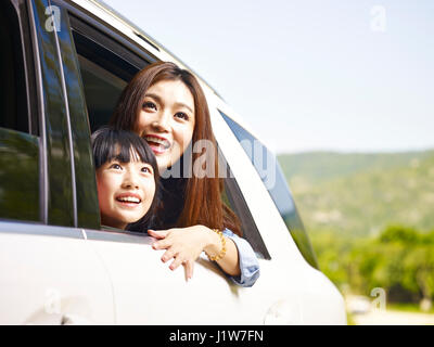 young asian mother and daughter sticking their heads out of rear window while riding in a car. Stock Photo