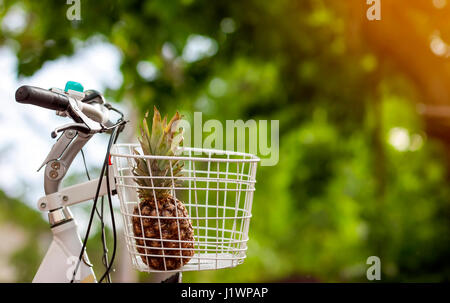 Pineapple in bike basket on green blurred background bokeh. Soft orange light effect. Stock Photo