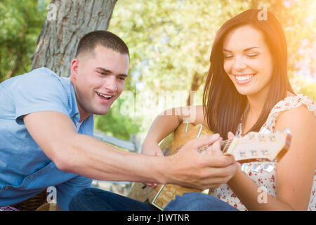 Handsome Young Man Teaching Mixed Race Girl to Play Guitar at the Park. Stock Photo