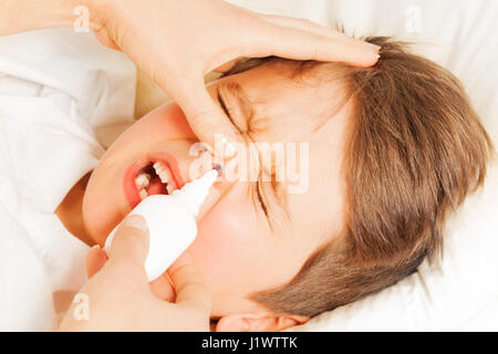 Close-up portrait of sick kid boy crying while mother spraying him nasal spray or drops in nose