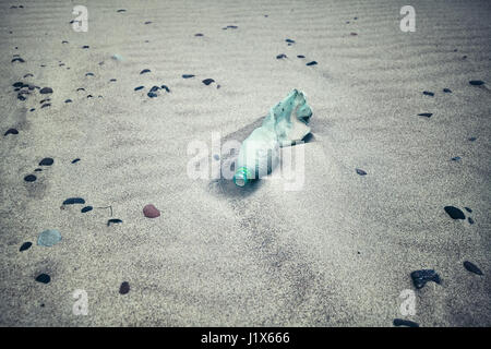 Color toned picture of an empty plastic bottle left on a beach, selective focus. Stock Photo