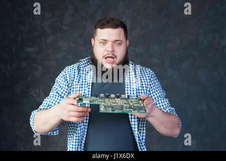 Male computer engineer blows off the dust from motherboard. Electronic devices repairing technology and service support Stock Photo