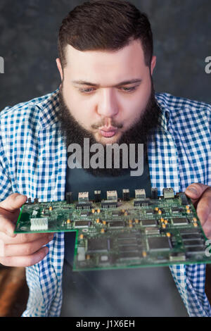 Male computer engineer blows off the dust from motherboard. Electronic devices repairing technology and service support Stock Photo