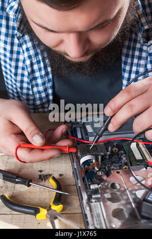 Male engineer hands diagnostics laptop with multimeter closeup view. Electronic devices repairing technology Stock Photo