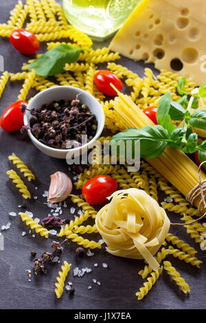 Ingredients for cooking Italian pasta - spaghetti, fusilli, fettuccine, basil, cherry tomato, garlic, pepper and cheese. Top view with space for text. Stock Photo