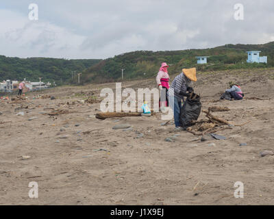 Shimen, Taiwan - October 03, 2016: Women in hats and masks on  faces cleaning up a beach by the ocean Stock Photo