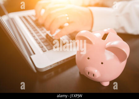 Piggy Bank Near Male Hands Typing on Laptop Computer. Stock Photo