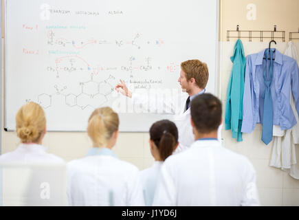 Young male chemical teacher explain lesson to his students in front of blackboard Stock Photo