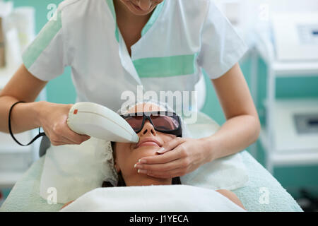 Beautician giving laser epilation treatment to young woman's face at beauty clinic, hairless smooth and soft skin Stock Photo