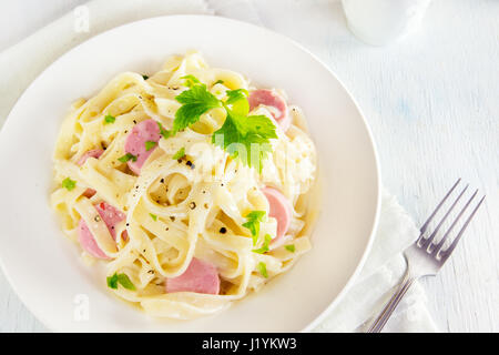 Alfredo tagliatelle pasta with sausages and greens on white plate - homemade creamy pasta Stock Photo