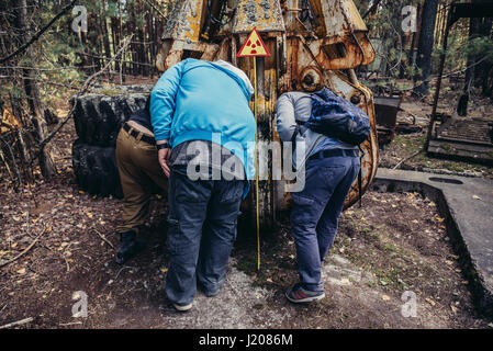 Tourists examine irradiated scrap bucket in Pripyat city of Chernobyl Nuclear Power Plant Zone of Alienation around nuclear reactor disaster, Ukraine Stock Photo