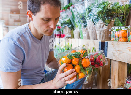 Young man picking holding plastic boxes with mandarin oranges in store Stock Photo