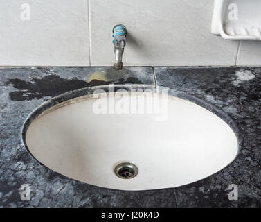 Dirty basin with the stained metal faucet in the public toilet of the urban park. Stock Photo