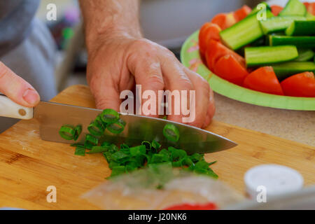 Cut green onion with a kitchen knife on a wooden cutting board. Fresh green onions on a cutting board. Cutted Green Onions On Wooden Cutting Board Stock Photo