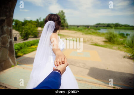 Beautiful young woman bride holds the hand of a man in outdoors. Follow me Stock Photo