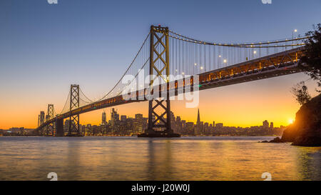 Classic panoramic view of San Francisco skyline with famous Oakland Bay Bridge illuminated in beautiful golden evening light at sunset in summer, San  Stock Photo