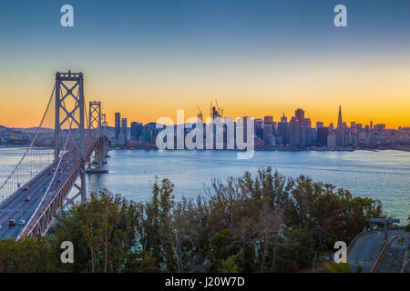 Classic panoramic view of famous Oakland Bay Bridge with the skyline of San Francisco illuminated in beautiful twilight with sunset glow in summer, Ca Stock Photo