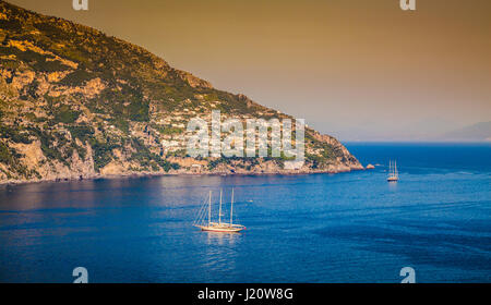 Panorama view of sailing yachts on the Mediterranean Sea at famous Amalfi Coast in beautiful golden evening light at sunset in summer, Campania, Italy Stock Photo