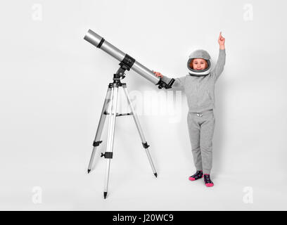 Happy child girl dressed in an astronaut costume standing beside the telescope Stock Photo