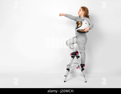 Happy child girl dressed in an astronaut costume standing on stepladder Stock Photo