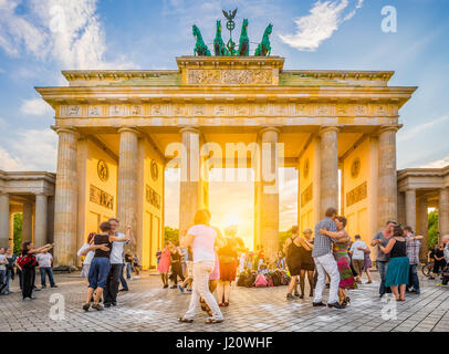 People dancing in front of famous Brandenburg Gate, a symbol for peace and unity and historic landmark, in golden evening light at sunset, Berlin Stock Photo