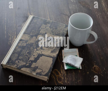 White cup, teabag and book on brown wooden table Stock Photo