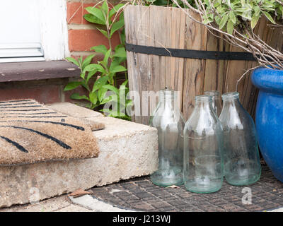 close up cool and modern shot of some glass milk bottles glasses outside empty no milk next to front door step and matt dairy retro vintage food ingre Stock Photo