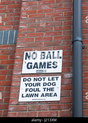 a sign outside up on the wall white and black saying no balls games do not let your dog foul the lawn area warning considerations laws restrictions si Stock Photo