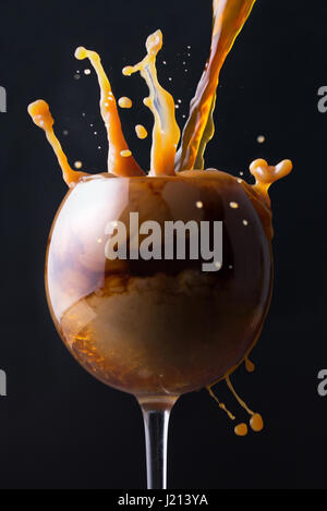 Splashes of coffee with milk in a glass on a black background Stock Photo