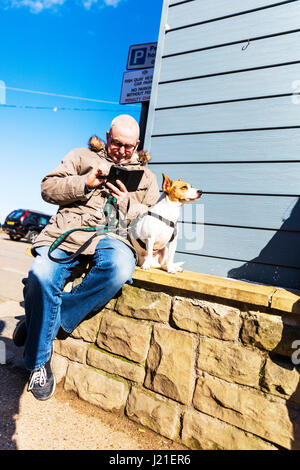 Man on phone with dog man using phone dog waiting patiently man stopped to use phone old man using smartphone UK England man using smartphone Stock Photo