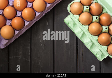 Brown chicken eggs in purple and light green carton over black wooden background Stock Photo
