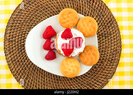 Fresh Red Raspberries on a white artistic plate / Red Fresh Raspberries on a white artistic plate with cookies, rosemary, chocolate and cream in the b Stock Photo