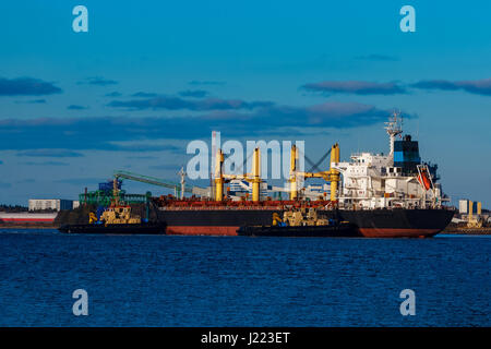 Black cargo ship mooring at the port with tug ship support Stock Photo