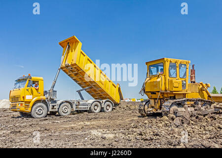 View on heavy bulldozer while he moving, leveling ground at construction site.  Heavy wheels are working at construction site. Stock Photo