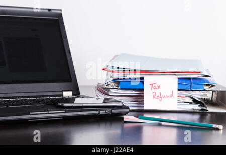 Handwritten note with tax return, refund text, formas and papers, notebook and laptop with mobile phone, cash on the table Stock Photo