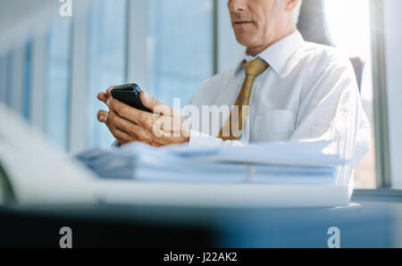 Cropped shot of senior business man sitting at his desk using mobile phone. Focus on hands of senior man reading text message on cell phone. Stock Photo